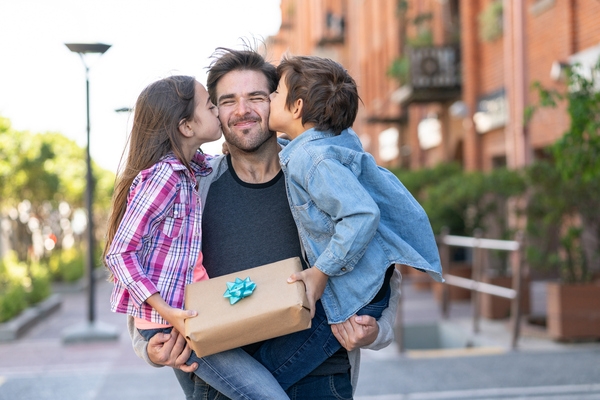 father holding kids on sidewalk while they give him a gift for fathers day