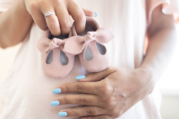 woman holding baby shoes over pregnant belly