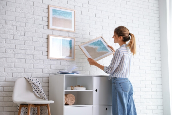 woman hanging picture on brick wall